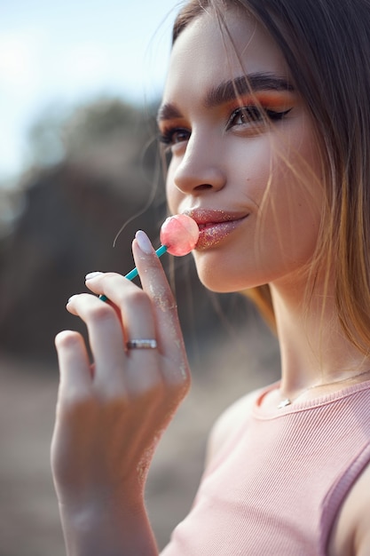 Hermosa mujer lamiendo un primer plano de piruleta. Sombras rojas en los ojos de una niña, maquillaje profesional, cosmética natural.