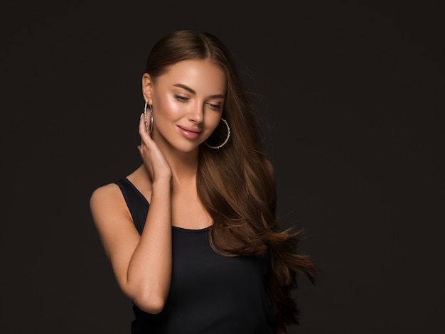 Hermosa mujer con largo cabello rizado saludable morena aretes vestido negro fondo negro