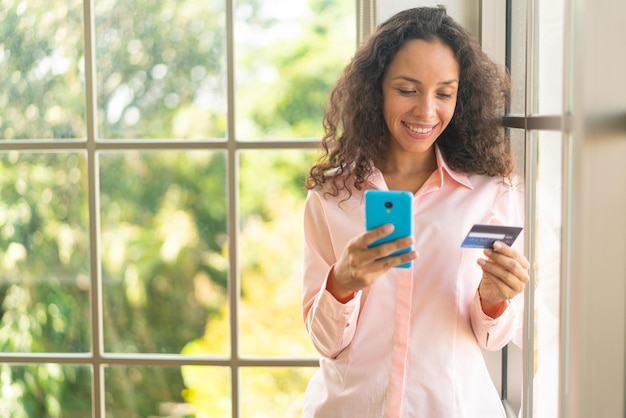 hermosa mujer latina usando un teléfono inteligente con una tarjeta de crédito en la mano