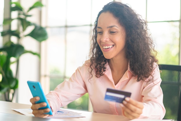 hermosa mujer latina usando un teléfono inteligente con una tarjeta de crédito en la mano