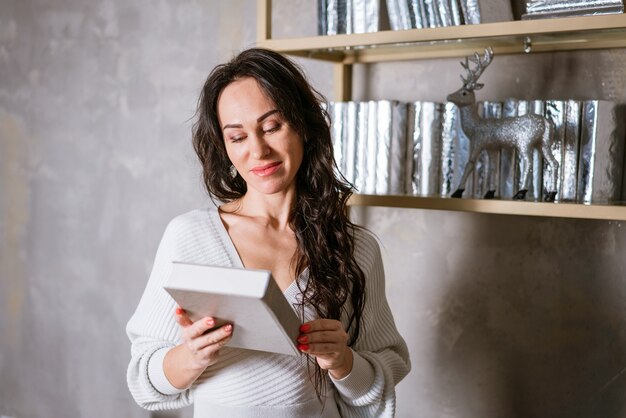 Hermosa mujer lee un libro cerca de la estantería chica morena caucásica con un vestido ligero se encuentra con un libro ...