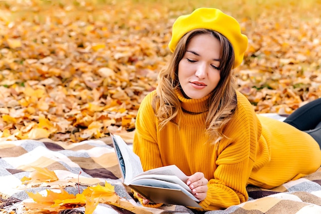Una hermosa mujer lee un libro en otoño Retrato de una hermosa morena leyendo un libro en el parque