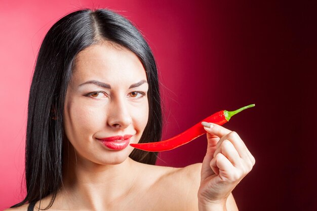 Foto hermosa mujer en lencería de encaje negro posando en estudio con fondo rojo ella está jugando con chile