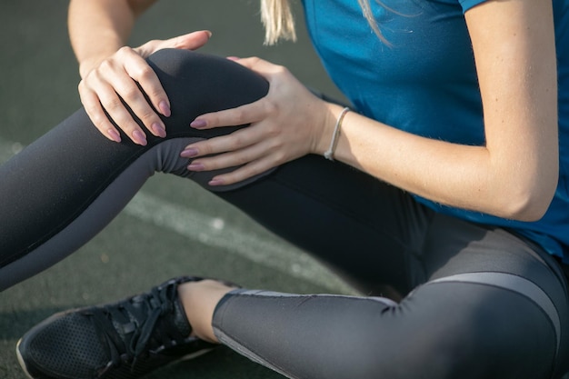 Hermosa mujer con lesión en la rodilla en la pista de atletismo de cerca. Concepto de salud y deporte. botella deportiva verde para beber