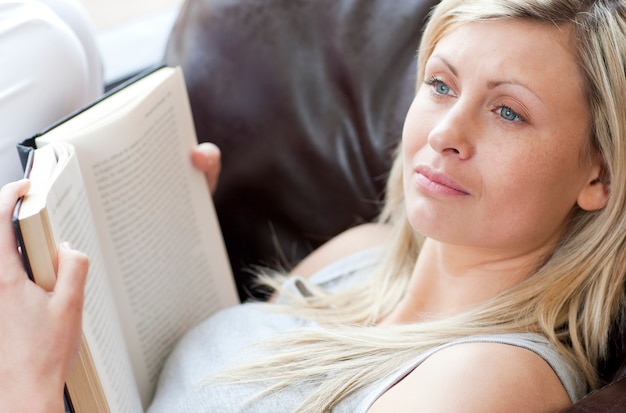 Hermosa mujer leyendo un libro sentado en un sofá