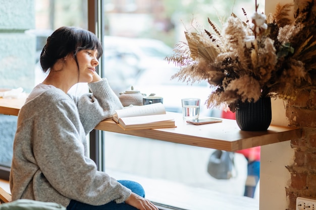 Hermosa mujer leyendo literatura romántica durante la pausa para el té en la cafetería con interior de loft, joven encantadora hipster chica pasar tiempo libre para autodidacta con libros sobre ocio