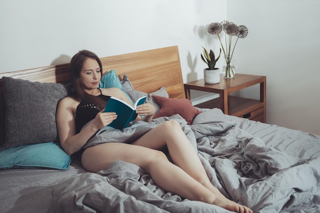 Foto hermosa mujer leyendo sentada en una cama cómoda