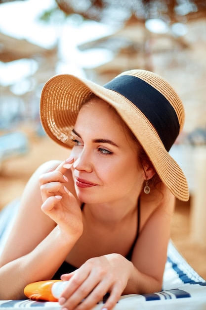 Hermosa mujer linda feliz aplicando crema bronceadora en la nariz con fondo de playa