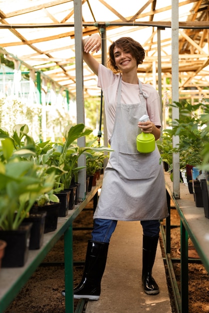 Hermosa mujer linda jardinero de pie sobre las plantas en flores de agua de invernadero