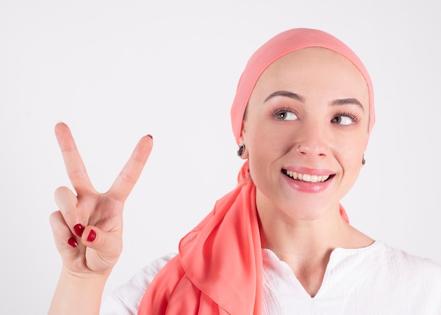 Hermosa mujer, luchadora contra el cáncer, lleva una bufanda rosa, hace el símbolo de la victoria con sus dedos