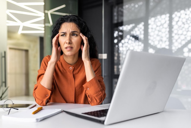 Foto hermosa mujer en el lugar de trabajo mujer hispana cansada con exceso de trabajo en el lugar de trabajo con dolor de cabeza severo