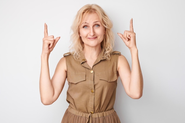 Hermosa mujer madura de 50 años señalando con el dedo hacia arriba demostrando el espacio vacío para el producto o el texto aislado en un fondo blanco de estudio