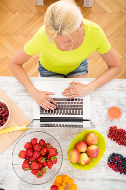Una hermosa mujer madura con una computadora portátil en la cocina con frutas.
