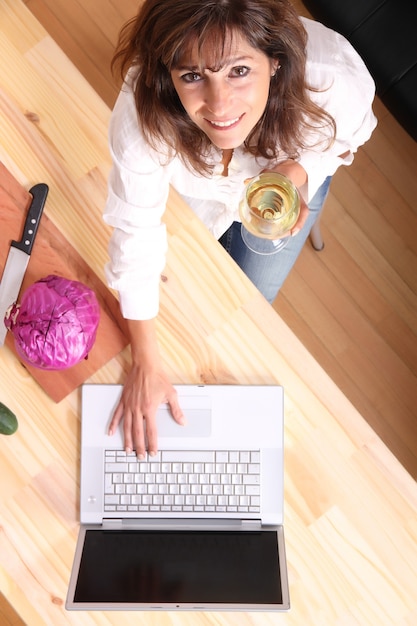 Una hermosa mujer madura cortando en la cocina con la ayuda de una computadora.