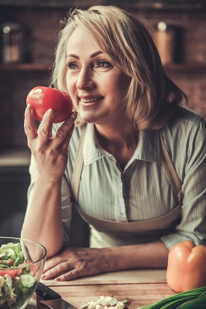 Hermosa mujer madura en delantal está oliendo tomate.