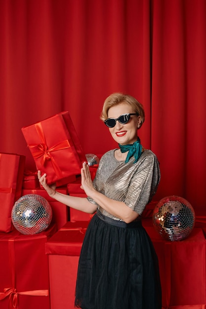 Hermosa mujer madura con estilo en gafas de sol con bola de discoteca y caja de regalo en el fondo de las cajas de regalo.