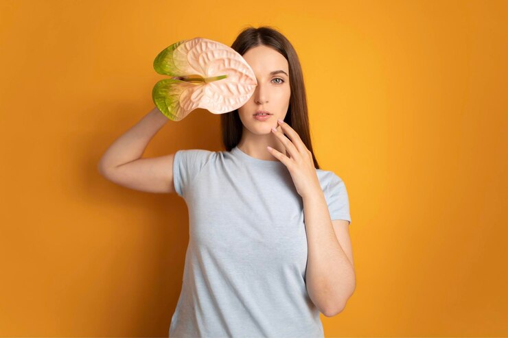Hermosa mujer con la mano cerca de la cara sosteniendo la flor de anthurium sobre fondo amarillo