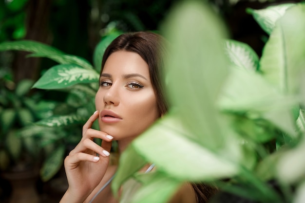 Hermosa mujer con maquillaje en los arbustos trópicos hojas de cerca