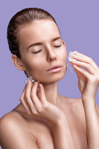 Hermosa mujer con maquillaje de aspecto natural con cubitos de hielo cerca de la cara