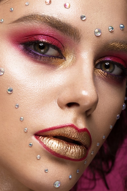 Hermosa mujer con maquillaje de moda brillante y corazón de cristales en la cara