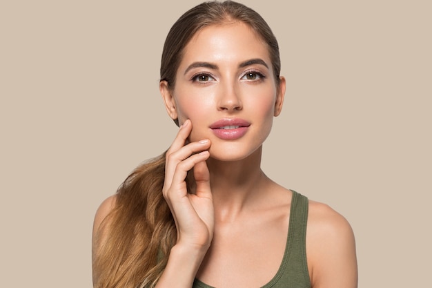 Hermosa mujer con maquillaje natural cosmético diario casual tocando su rostro. Fondo de color Marrón