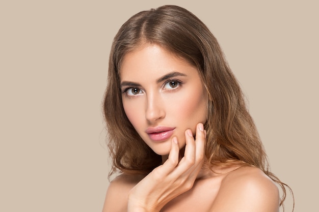 Hermosa mujer con maquillaje natural cosmético diario casual tocando su rostro. Fondo de color Marrón