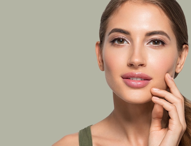 Hermosa mujer con maquillaje natural cosmético diario casual tocando su rostro. Fondo de color Verde