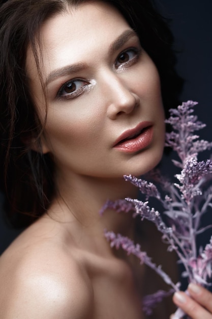 Hermosa mujer con un maquillaje natural ligero y una piel perfecta con flores en la mano Rostro de belleza