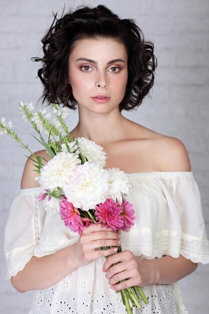 Hermosa mujer con un maquillaje natural ligero y una piel perfecta con flores en la mano Rostro de belleza