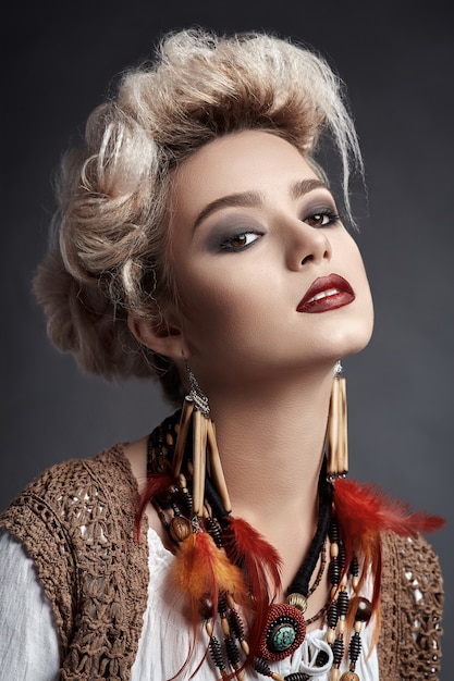 Hermosa mujer con maquillaje de ojos ahumados y aretes y collar de plumas