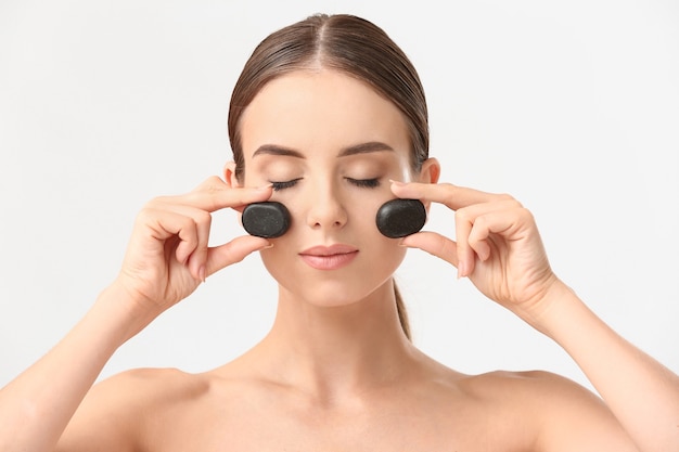 Hermosa mujer masajeando su rostro con piedras calientes fondo blanco.