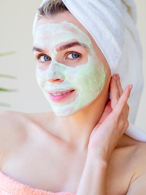 Hermosa mujer con máscara de arcilla facial natural verde. Retrato de cerca. Tocando su cara.