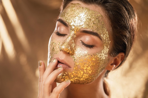 Hermosa mujer con máscara dorada brillante en la cara para el tratamiento de la piel