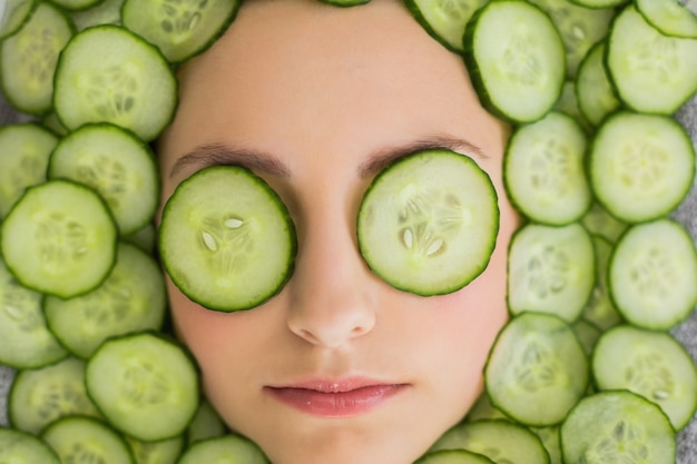 Hermosa mujer con máscara facial de rodajas de pepino en la cara