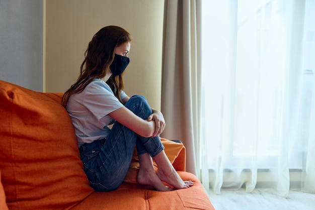 Hermosa mujer con máscaras médicas negras encerrada en casa en el sofá Cuarentena