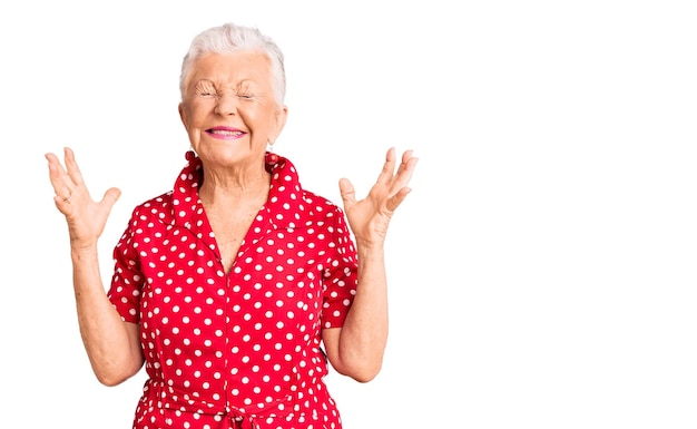 Foto hermosa mujer mayor con ojos azules y cabello gris con un vestido rojo de verano celebrando loco y loco por el éxito con los brazos levantados y los ojos cerrados gritando emocionados. concepto de ganador