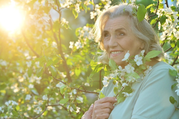 Hermosa mujer mayor posando cerca de un árbol floreciente