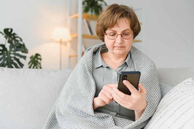 Hermosa mujer mayor en ropa casual usando su teléfono inteligente mientras está sentado en el sofá en casa