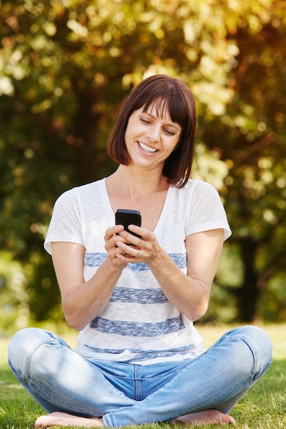 Hermosa mujer mayor sentada en el césped con teléfono inteligente