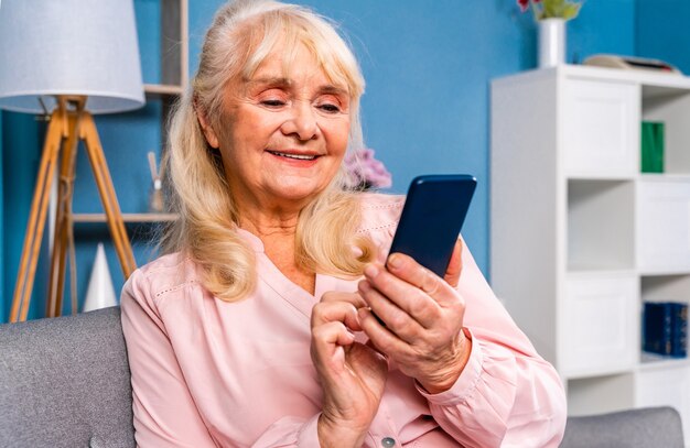 Hermosa mujer mayor sentada sola en casa y usando un dispositivo de teléfono inteligente para conectarse a internet