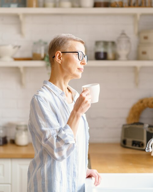 Hermosa mujer mayor con una taza de café o agua rure mirando en la ventana mientras disfruta de un nuevo día en