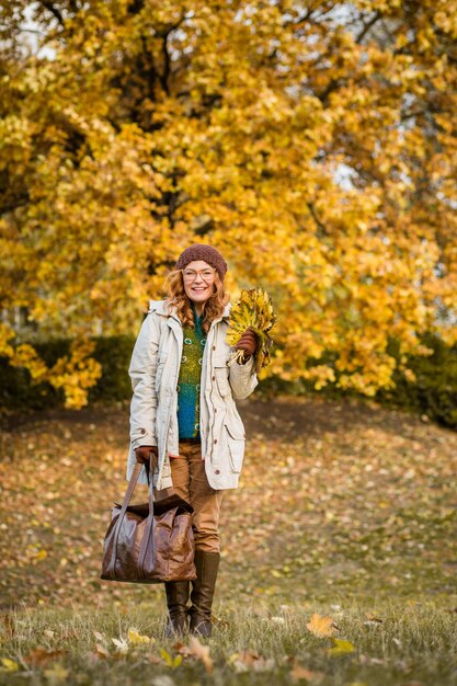 Hermosa mujer de mediana edad comunicándose con otoño amarillo Mujer feliz sosteniendo una bolsa de cuero y caminando en la naturaleza