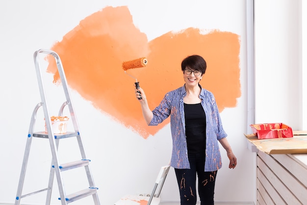 Hermosa mujer de mediana edad pintando la pared con rodillo de pintura. Retrato de una joven hermosa