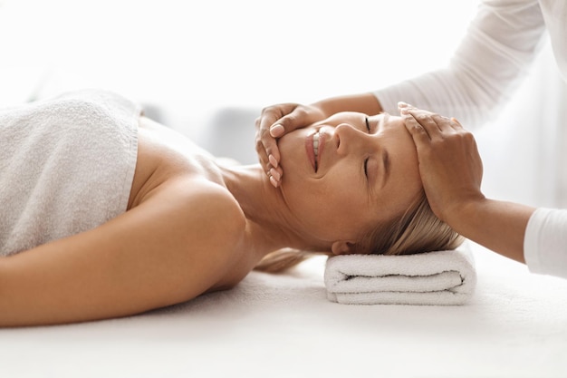 Hermosa mujer de mediana edad recibiendo tratamiento de masaje facial en el salón de spa