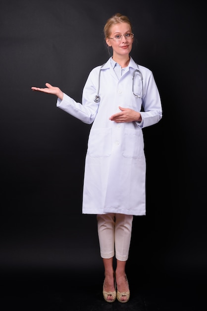 Hermosa mujer médico con cabello rubio contra la pared negra