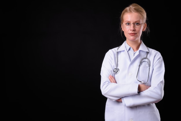 Hermosa mujer médico con cabello rubio contra la pared negra