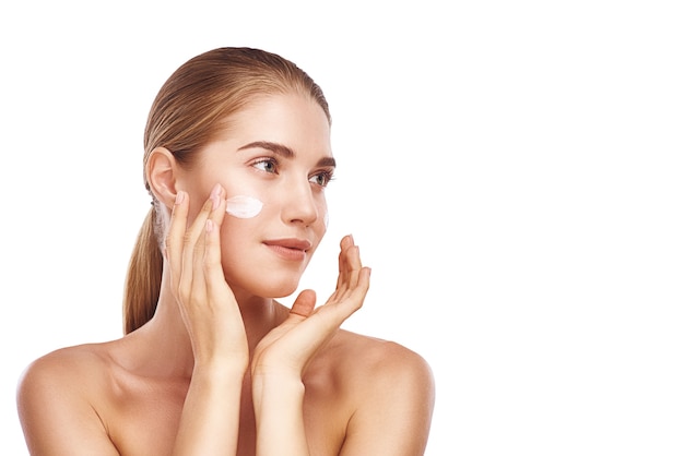 Hermosa mujer mejilla izquierda con crema facial de cerca foto de estudio sobre fondo blanco. Cabello claro, ojos grises