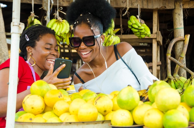 Una hermosa mujer del mercado africano y su cliente se sienten sorprendidos por lo que tienen en su teléfono celular