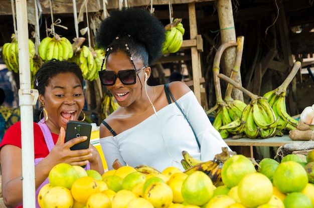 Una hermosa mujer del mercado africano y su cliente se sienten sorprendidos por lo que tienen en su teléfono celular