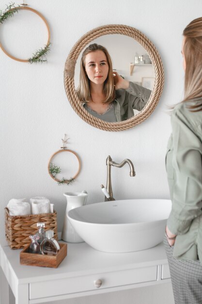 Una hermosa mujer se mira en el espejo del baño por la mañana y sonríe. Perfumería